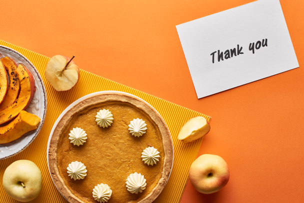 top view of pumpkin pie with thank you card on orange background with apples - Photo, Image