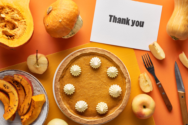 Draufsicht auf köstlichen Kürbiskuchen mit Dankeskarte auf orangefarbenem Hintergrund mit Äpfeln - Foto, Bild