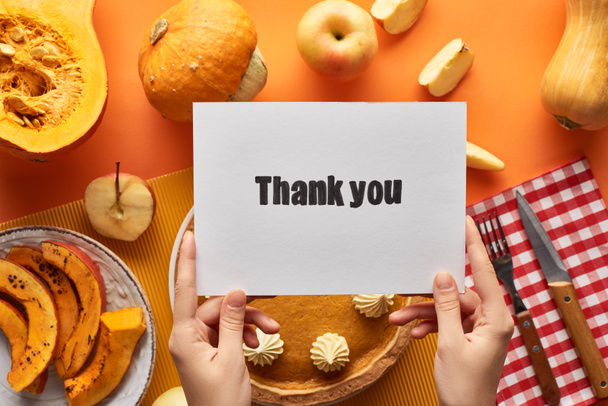 cropped view of woman holding thank you card near pumpkin pie on orange background - Фото, изображение