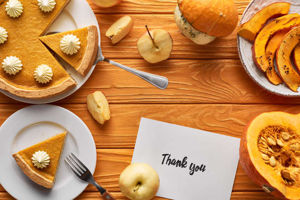Draufsicht auf köstlichen Kürbiskuchen, Äpfel und Dankeskarte auf orangefarbenem Holztisch - Foto, Bild