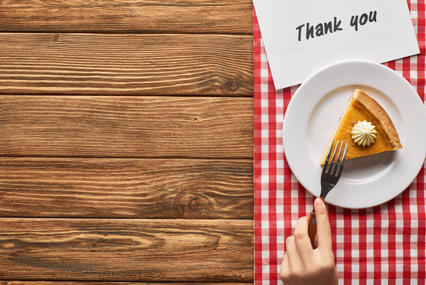 bijgesneden weergave van vrouw eten pompoen pie op geruite servet met dank u kaart op houten tafel - Foto, afbeelding