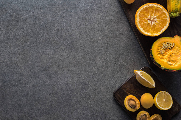 top view of yellow fruits and vegetables on wooden cutting boards on grey textured background with copy space - Fotó, kép