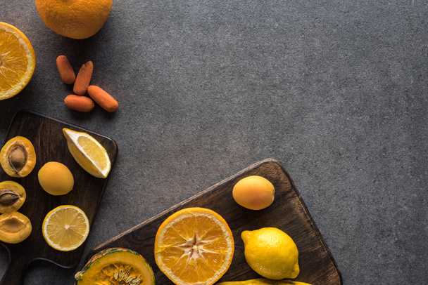 vista superior de frutas e legumes amarelos em tábuas de corte de madeira em fundo texturizado cinza com espaço de cópia
 - Foto, Imagem