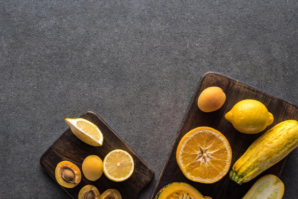 bovenaanzicht van geel fruit en groenten op houten snijplanken op grijze textuur achtergrond met kopieerruimte - Foto, afbeelding