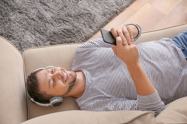 Muž s mobilním telefonem a sluchátky relaxačně doma - Fotografie, Obrázek