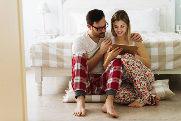 Young attractive couple using digital tablet in bedroom - Фото, изображение