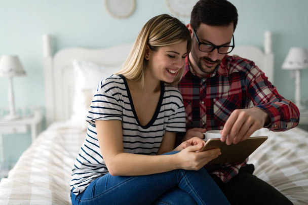 Young attractive couple using digital tablet in bedroom - Foto, afbeelding