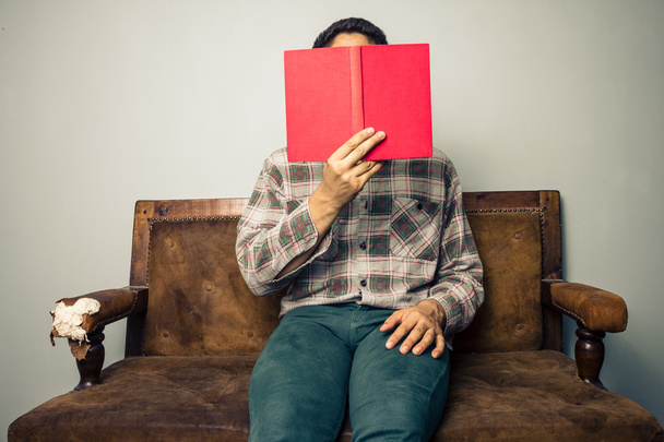 Человек прячется за книгой на старом диване
 - Фото, изображение
