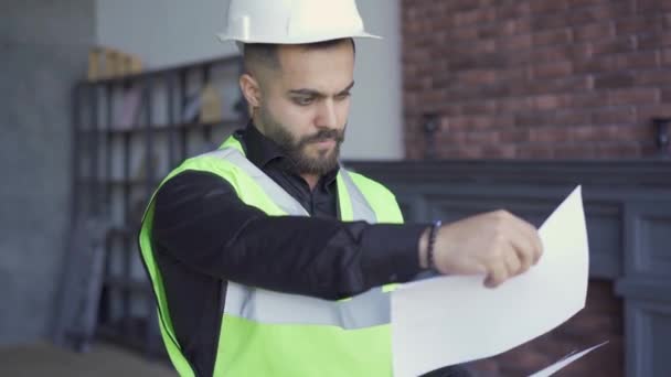 Builder in the helmet and green jacket examining drawings. Professional at work. Man looking through papers. - Metraje, vídeo
