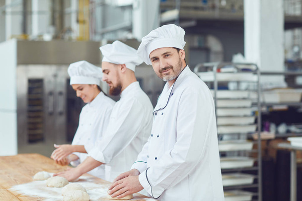 Baker with dough in hand in the bakery. - Fotó, kép