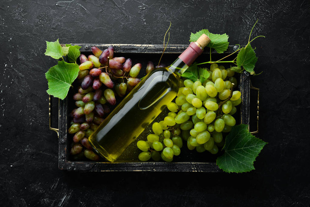 Bottle of white wine and fresh grapes on a black stone table. Top view. Free space for your text. - Valokuva, kuva