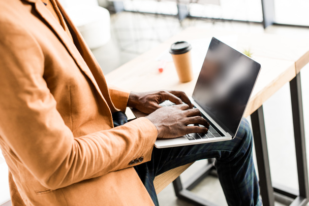 vista recortada del hombre de negocios afroamericano sentado en el escritorio y utilizando el ordenador portátil
 - Foto, imagen