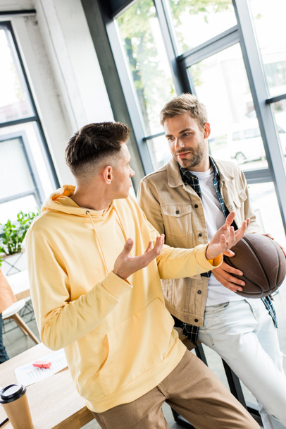 молодий бізнесмен жестикулює під час розмови з колегою, що тримає волейбол
  - Фото, зображення