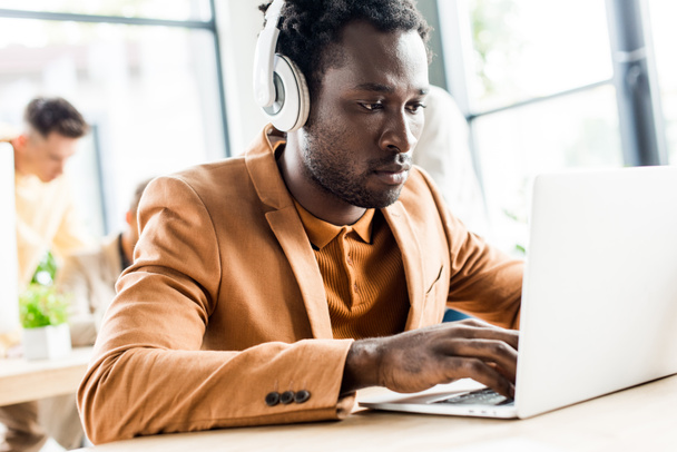 handsome african american businessman in headphones using laptop - Foto, afbeelding