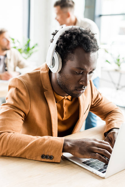νεαρός, όμορφος Αφροαμερικάνος επιχειρηματίας με ακουστικά χρησιμοποιώντας φορητό υπολογιστή - Φωτογραφία, εικόνα