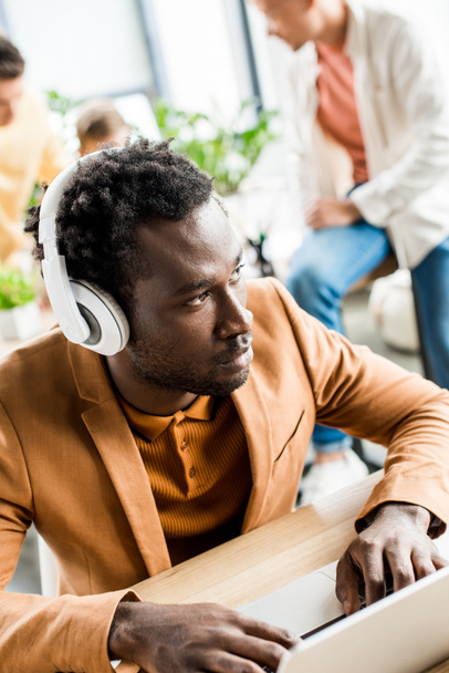 poważny afrykański amerykański biznesmen w słuchawkach za pomocą laptopa w biurze - Zdjęcie, obraz
