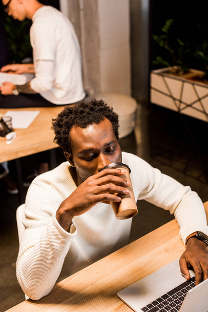 tired african american businessman drinking coffee to go while working at night in office - Foto, Imagem