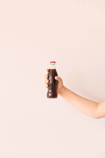 Female hand with bottle of cola on light background - Photo, Image