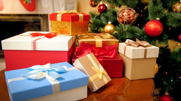 Closeup image of big heap of colorful Christmas gifts boxes and presents against decorated Christmas tree with garlands and balls - Photo, Image
