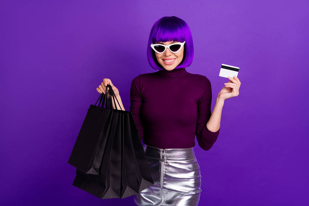 Portrait of charming consumer with eyeglasses eyewear holding packages wearing turtleneck silver skirt isolated over purple violet background - Fotoğraf, Görsel