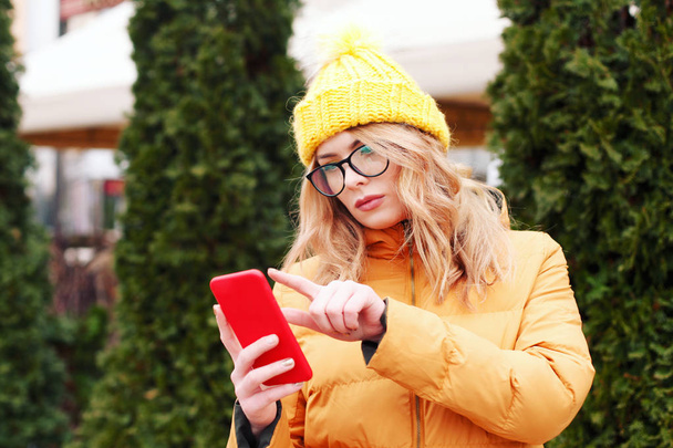 Frau in orangefarbenem Mantel im Winter mit Smartphone auf der Straße - Foto, Bild