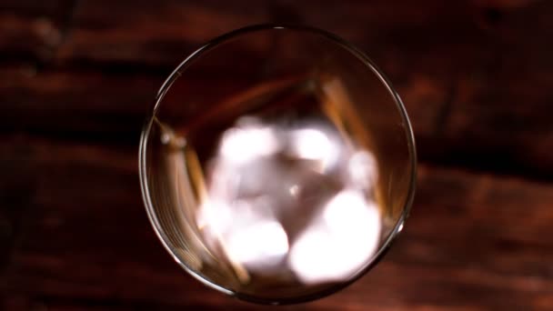 Super slow motion of falling ice cube into whiskey glass, top view. Filmed on cinema slow motion camera, 1000fps - Materiał filmowy, wideo