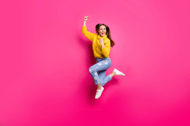 Full length photo of delighted lady jumping raising her fists screaming yeah feel lucky wearing yellow pullover denim jeans isolated over fuchsia background - Fotoğraf, Görsel