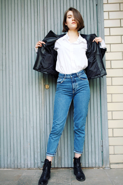 attractive woman posing near building in leather jacket - Фото, зображення