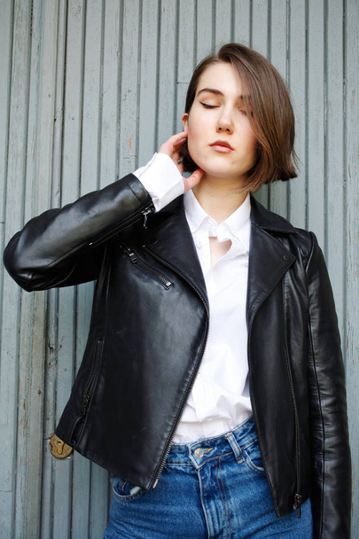 attractive woman posing near building in leather jacket - Φωτογραφία, εικόνα