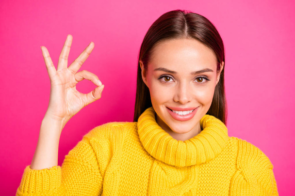 Close up photo of charming girl looking with toothy smile showing ok sign wearing yellow knitted jumper isolated over fuchsia background - Foto, Bild