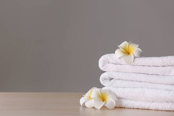 Stack of clean towels with flowers on table against grey background - Photo, Image