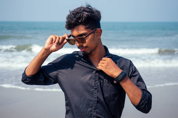 young hindu stylish man posing with sunglasses active beach vacation on semmertime happy Goa India beach. sunscreen spf protection concept. - Photo, Image