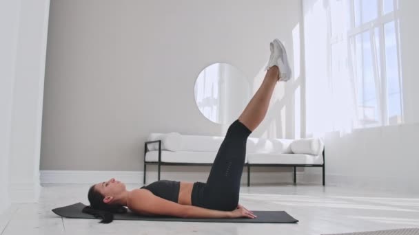 Sportswoman training at home. Fit female athlete doing toe touch single arm exercise lying on floor in white apartment - Felvétel, videó