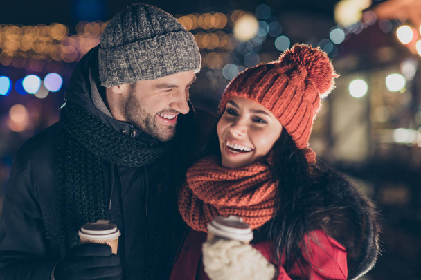 Photo of two funny people pair with hot beverage in hands spending x-mas evening together outdoors having magic free time wearing warm coats - 写真・画像