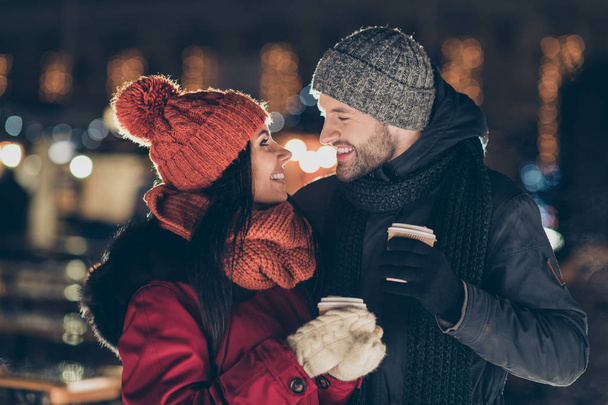 Photo of two affectionate people with hot tea beverage in hands celebrating x-mas eve in magic atmosphere wearing warm coats outside - Fotó, kép