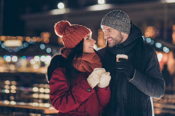 Photo of two people with hot tea beverage in hands celebrating x-mas eve in magic outdoors atmosphere wearing warm jackets - Photo, image