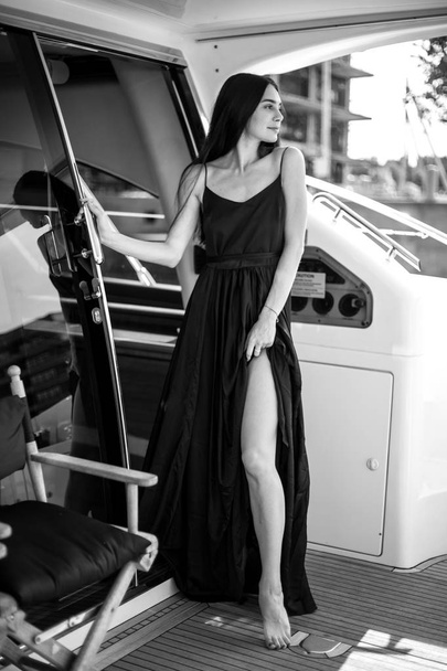 Young beautiful woman in a long silk black dress posing on a yacht. Luxurious life style, summer time - Photo, image