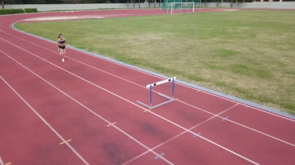Female athlete on track. Young runner running on track of stadium, jumps through barriers. Healthy life - Video
