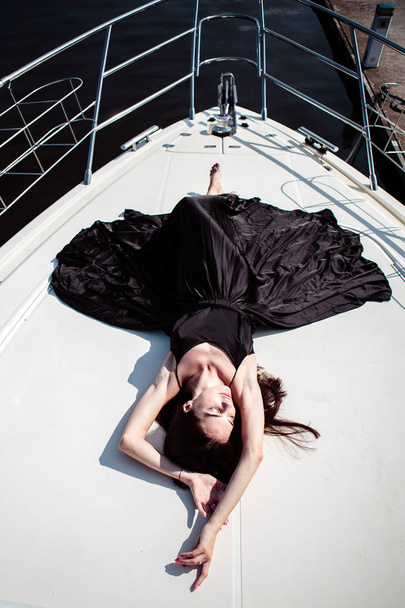 Uzun ipek siyah elbiseli genç güzel kadın bir yatta poz. Lüks yaşam tarzı, yaz saati - Fotoğraf, Görsel