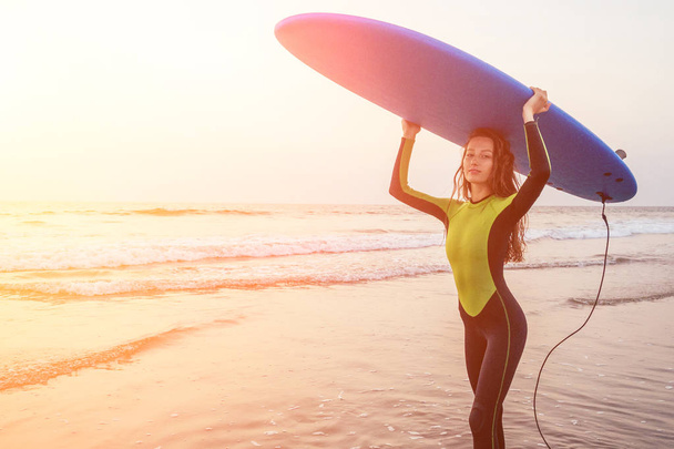 Beautiful woman in a diving suit for swimming surfing in the Indian Ocean on the background sunset sky and waves.professional surfer girl in a wetsuit doing sports at sea.extreme, adrenaline and youth - Foto, Bild