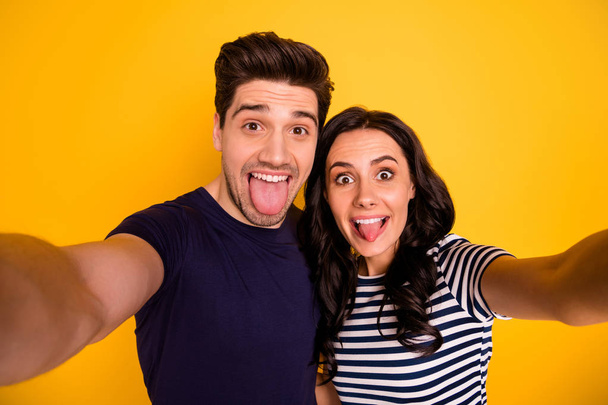 Self portrait of nice lovely charming couple of two people showing tongue while isolated with yellow background - Фото, изображение