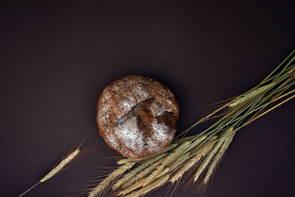 Brood en de oren van tarwe op een donkere achtergrond, bovenaanzicht. - Foto, afbeelding
