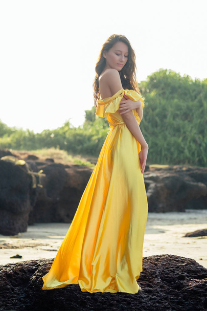 Красива жінка в жовтій шовковій сукні, що тече на пляжі
 - Фото, зображення
