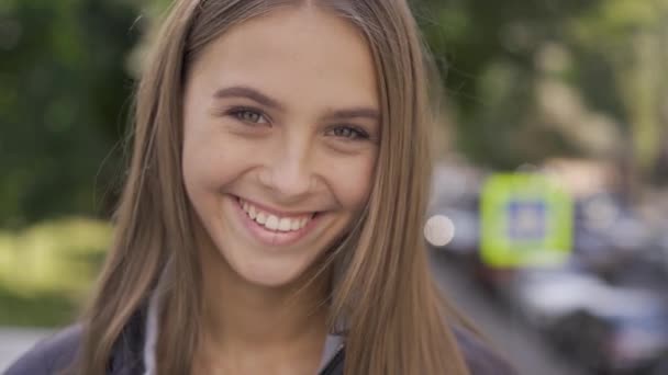 Close-up portrait of young caucasian woman with long hair smiling happily looking at the camera in the city street. Emotions, happiness, good mood - Záběry, video