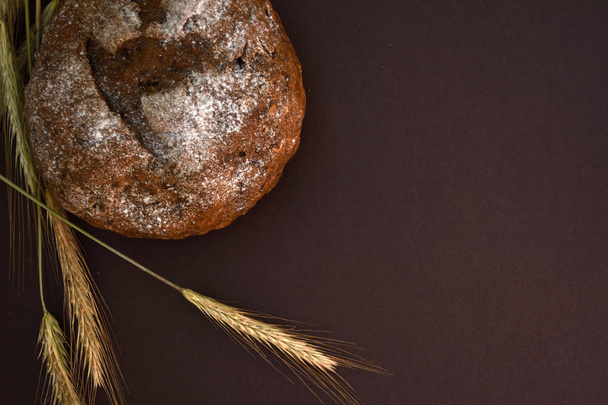 Loaf of bread and ears of wheat on a dark background, top view, copy space. - Photo, Image