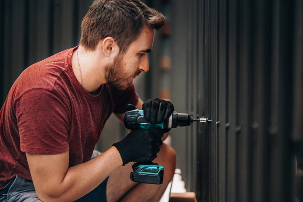 Handyman using a cordless screwdriver and drilling screws in metal fence - Fotoğraf, Görsel