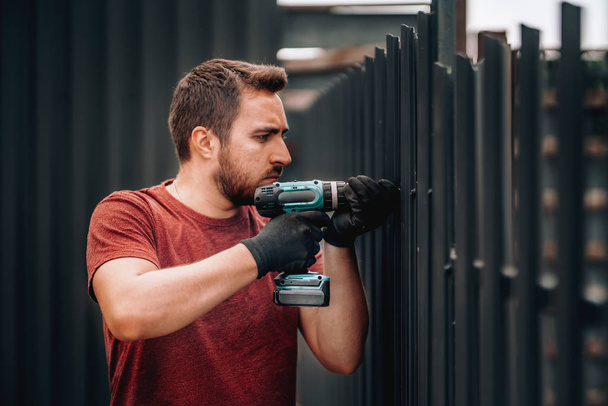 Caucasian construction man working with screwdriver on metal fence - Fotoğraf, Görsel