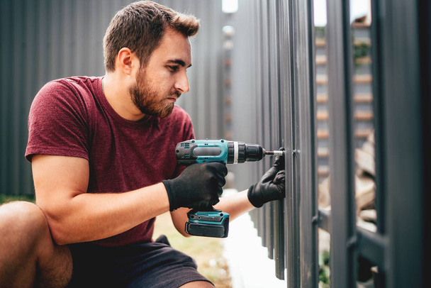 Caucasian construction man working with cordless electrical screwdriver on metal fence - Foto, Imagem