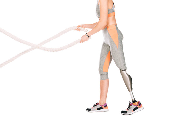 cropped view of disabled sportswoman with prosthetic leg training with ropes isolated on white - Zdjęcie, obraz
