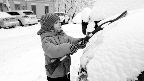 Foto da vicino di sorridente ragazzo carino felice in cappotto beige e cappello, divertirsi a giocare nella neve in inverno dopo la nevicata
 - Foto, immagini